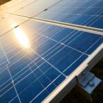 Close-up of monocrystalline solar photovoltaic panel cells showing the grid pattern and blue silicon surface with sun reflection.